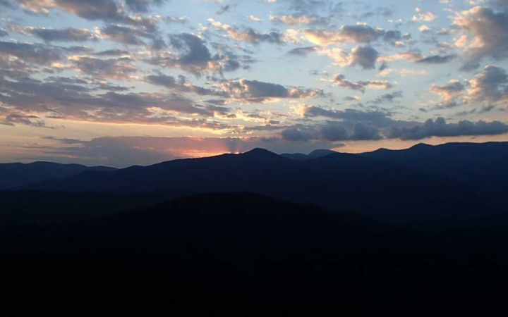 The sun is setting or rising behind a mountain range, illuminating the sky in blue, yellow and pink.